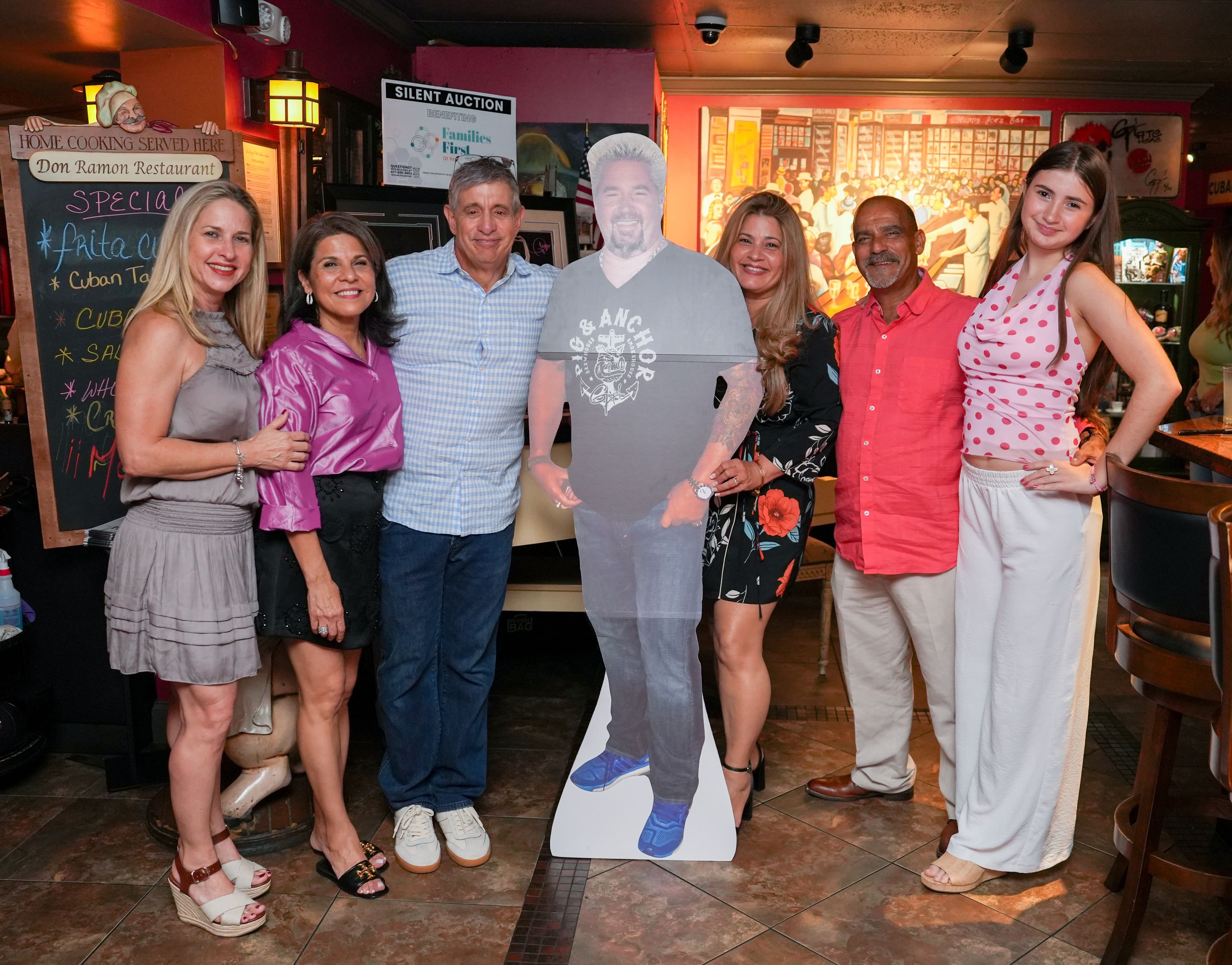 Six guests posed around the Guy Fieri cutout at the Families First silent auction, beside the specials board