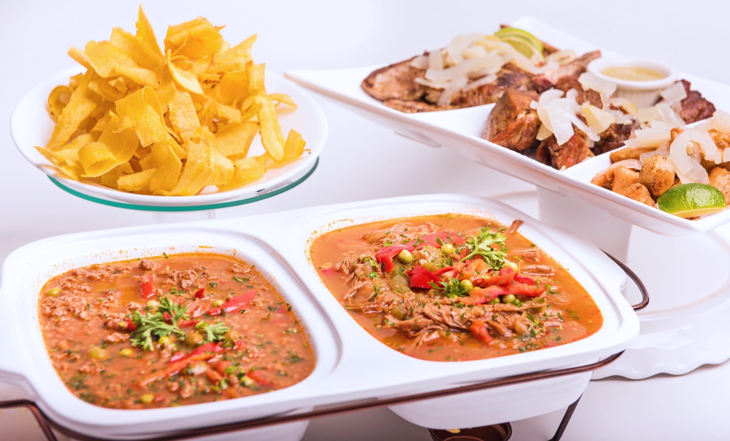 Picadillo and ropa vieja in a chafing dish beside a platter of pork, steak and chicken chunks and a stand of plantain chips